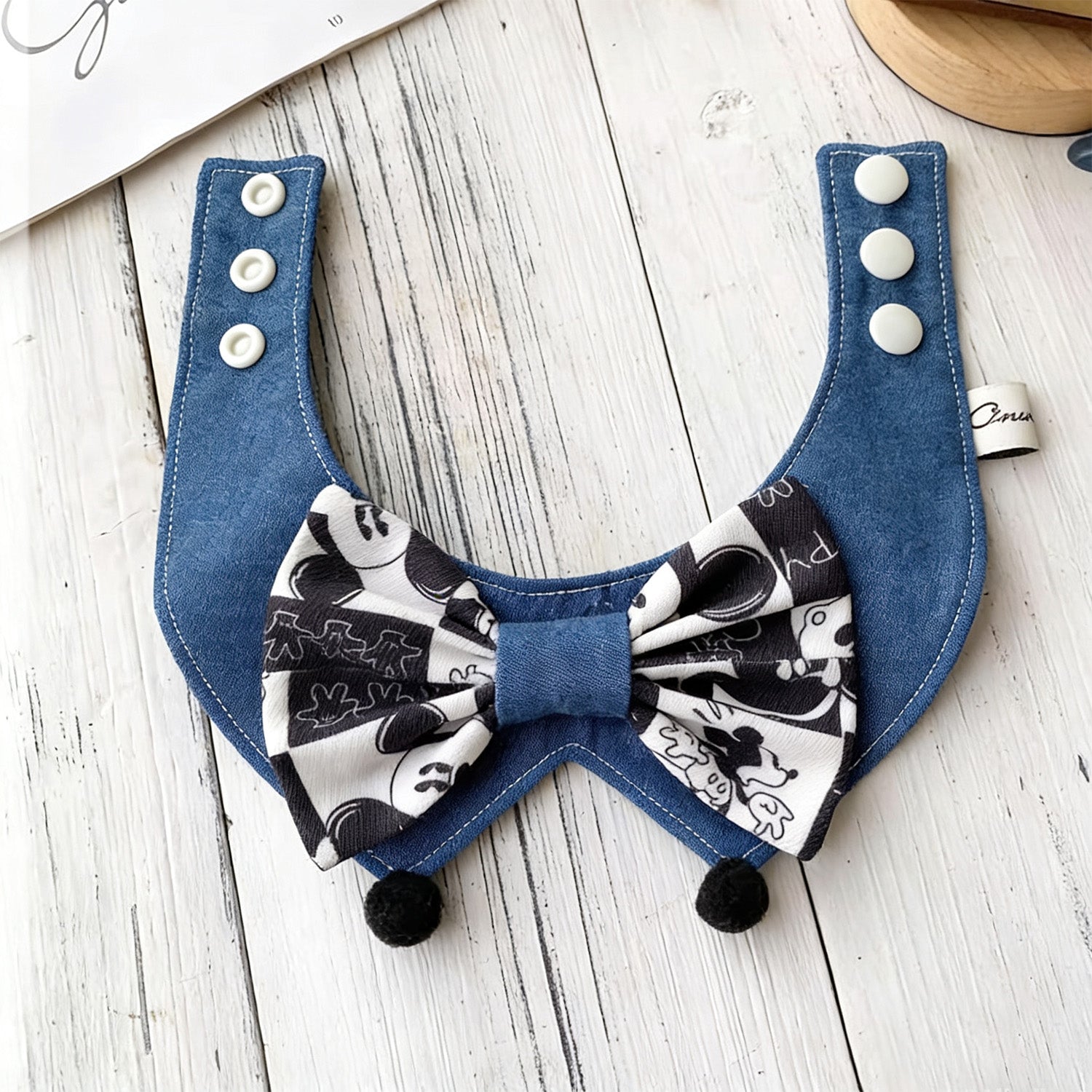 Black and white cartoon bow pet bandana collar with black pom-poms detail view
