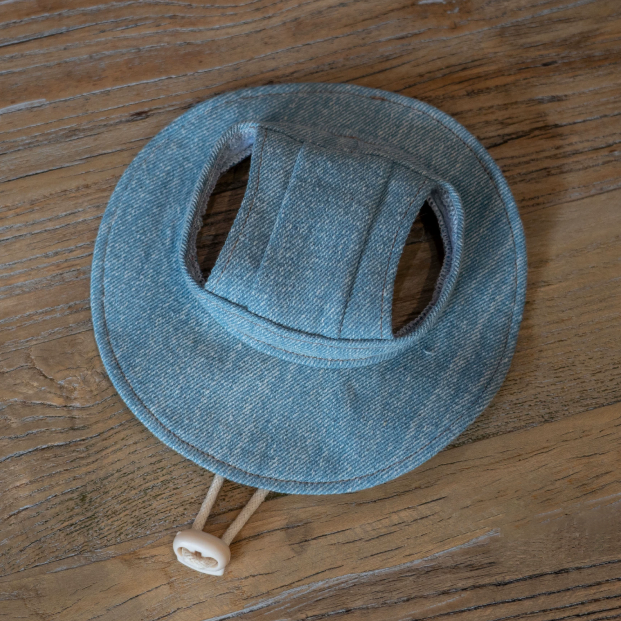 Close-up of GraviPaw light blue denim cat hat with adjustable strap on wooden surface