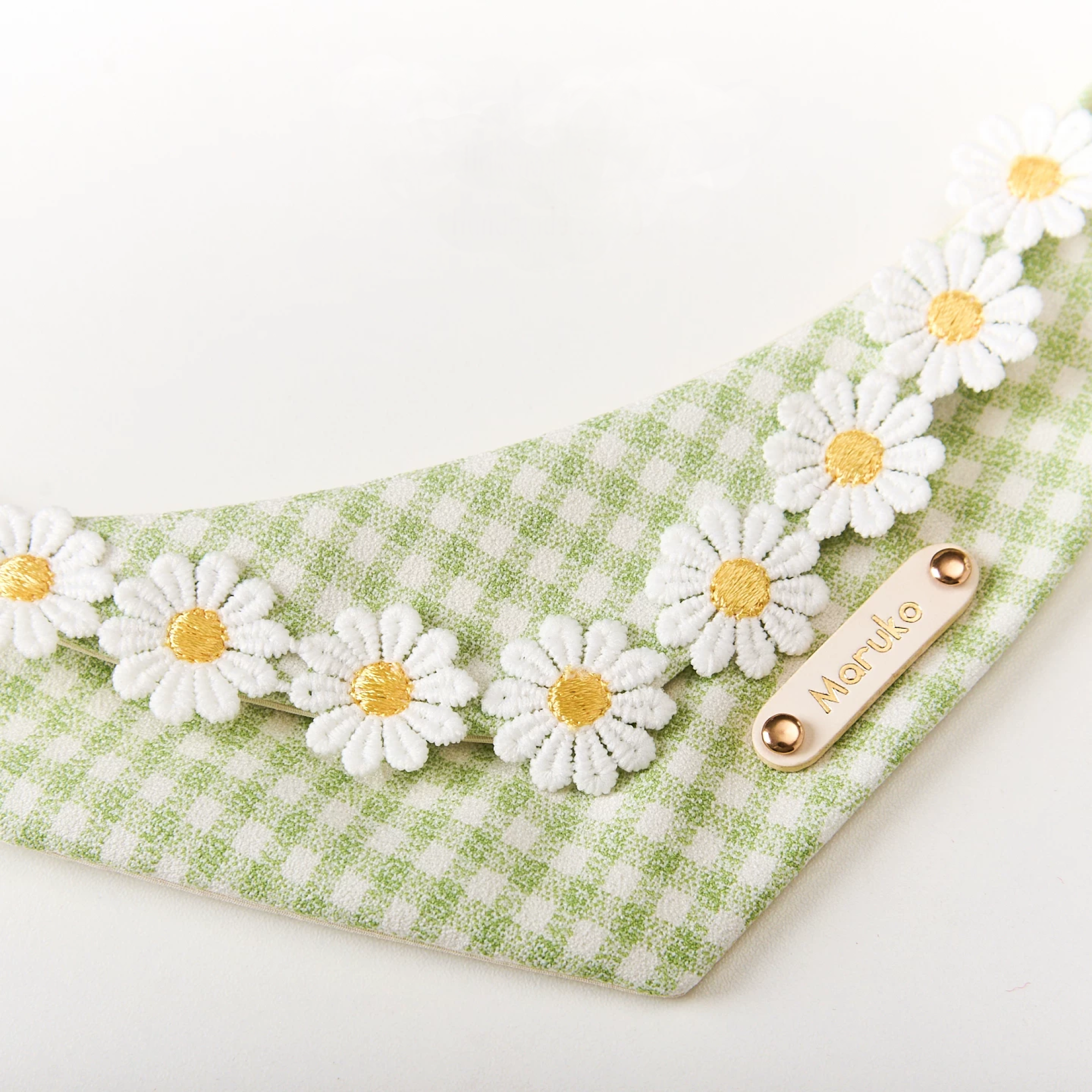 Detail of plush embroidered white daisies along the edge of green gingham pet bandana