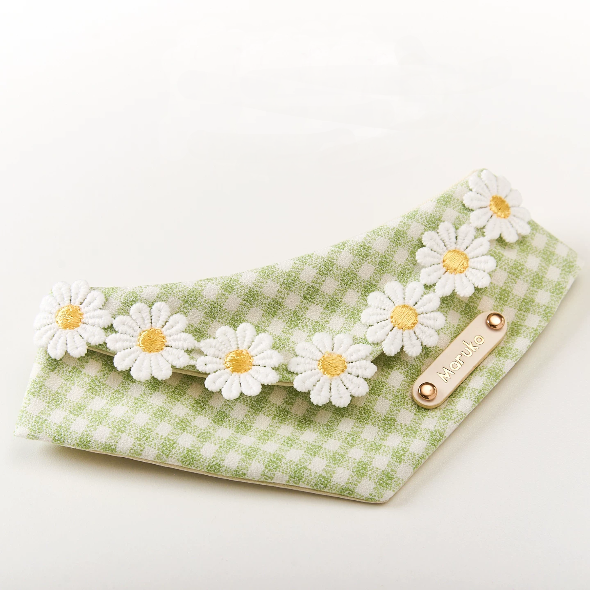 Close-up of personalized gold name plate on green gingham daisy pet bandana for cats and small dogs