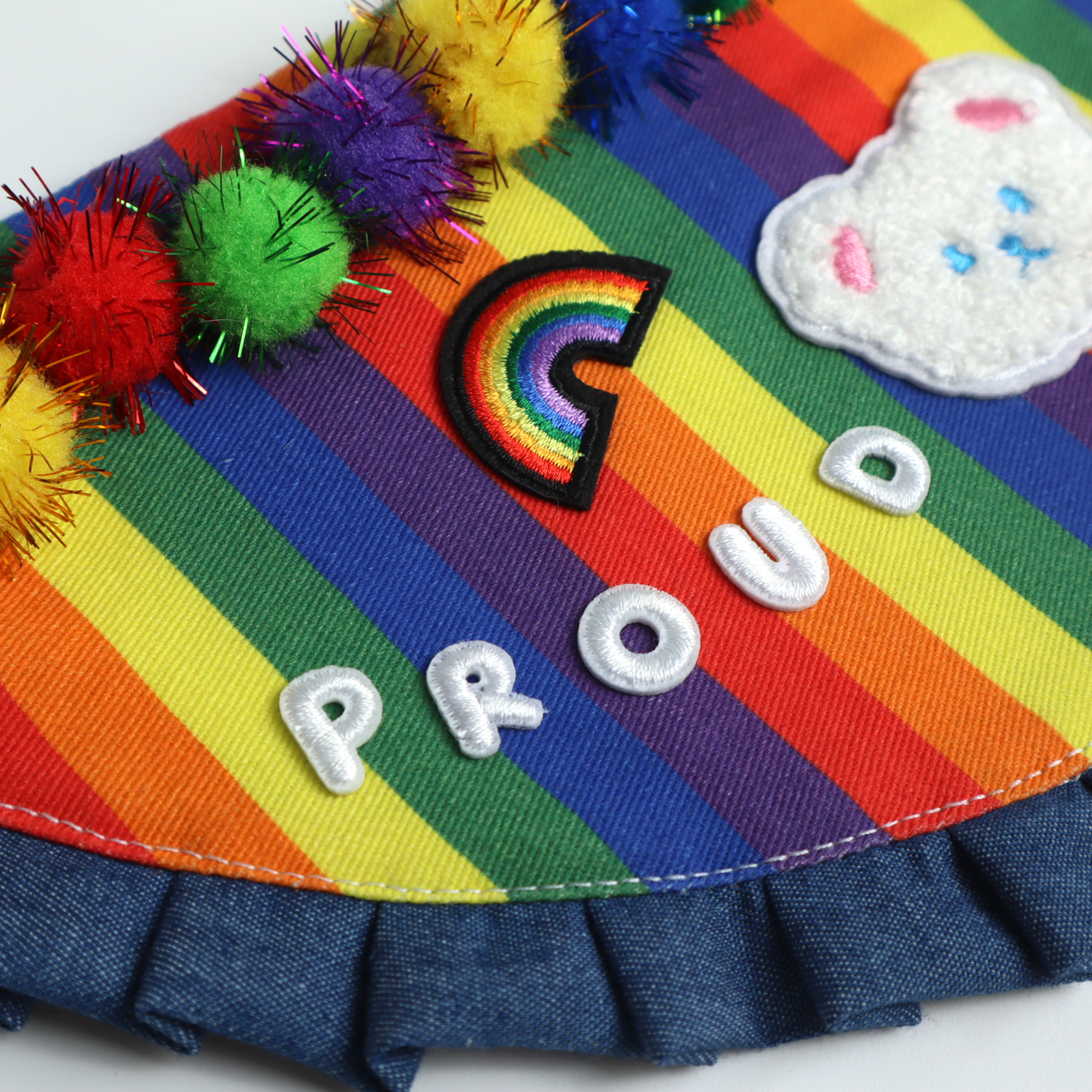 Flat lay of rainbow Pride pet bandana showing embroidered teddy face and "PROUD" text